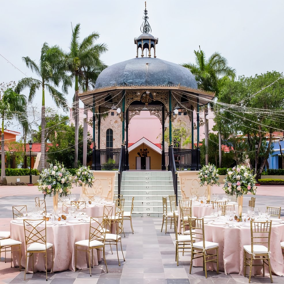 Destination wedding setup featuring round tables, gold chairs, and a gazebo in the scenic background.