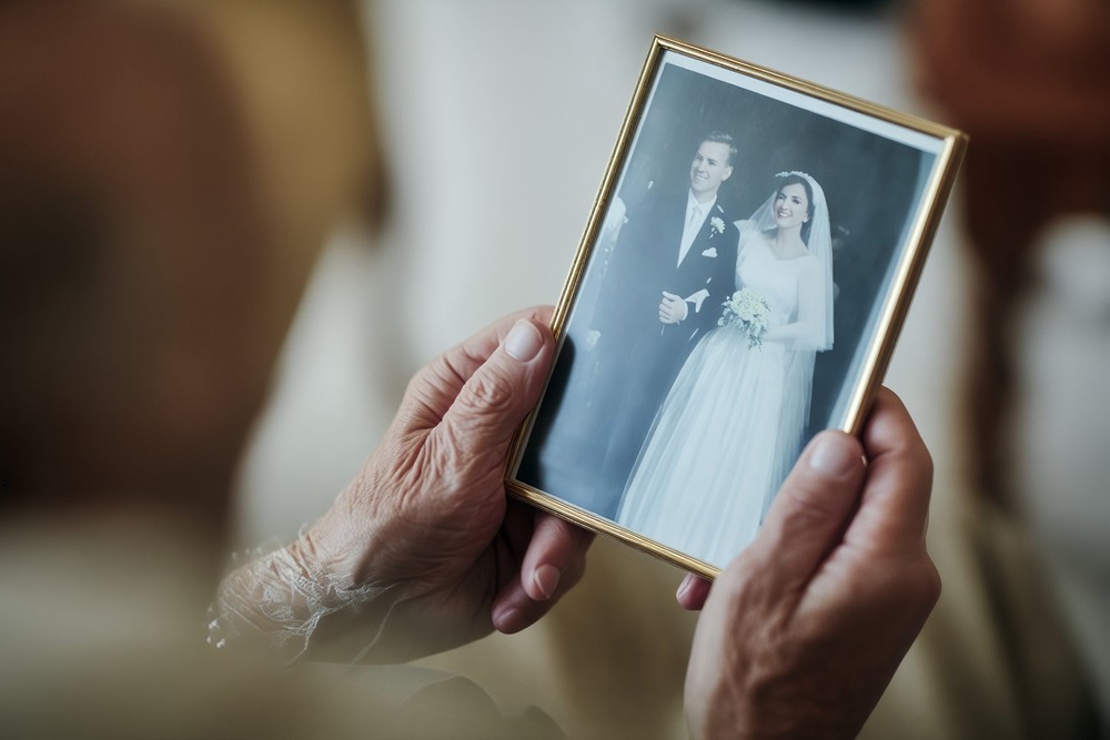 Aged hands gently hold a framed photograph, reminiscing about heartfelt wedding vows exchanged on their unforgettable destination wedding day.