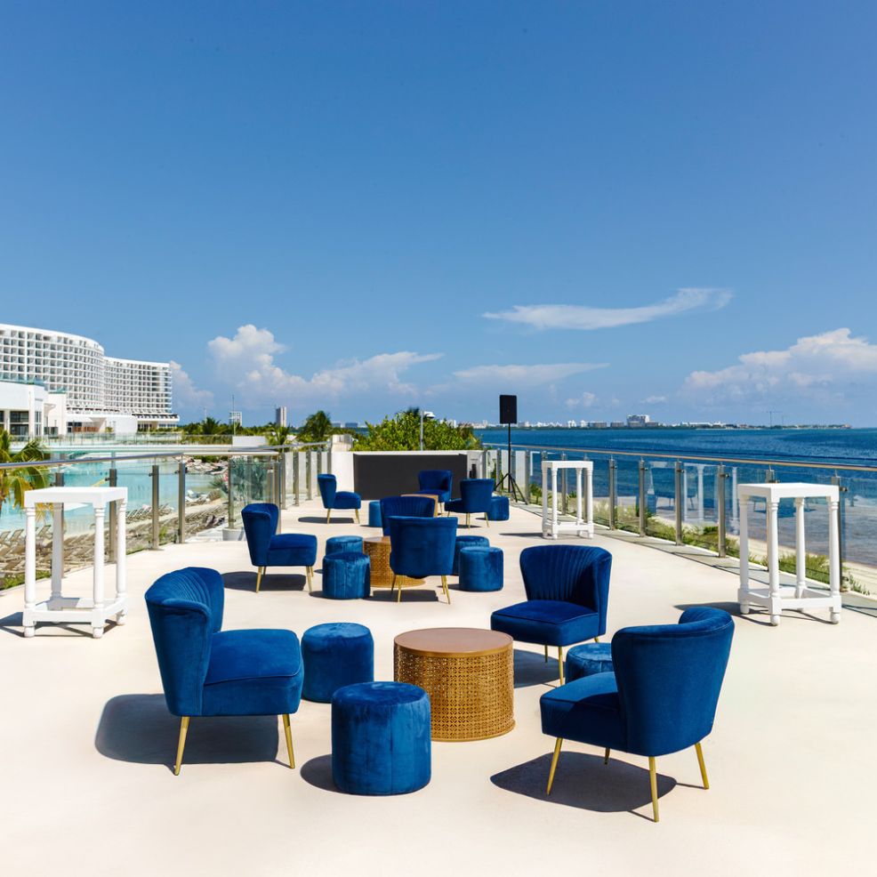 Blue chairs and tables set on a sunny terrace overlooking the ocean, perfect for a destination wedding.