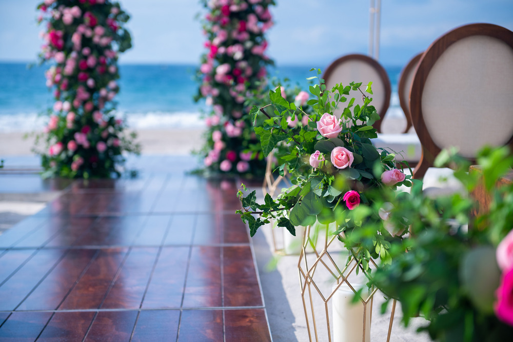 A beautiful destination wedding aisle by the beach, featuring pink florals, wooden chairs, and stunning ocean views—all part of an affordable destination wedding package.