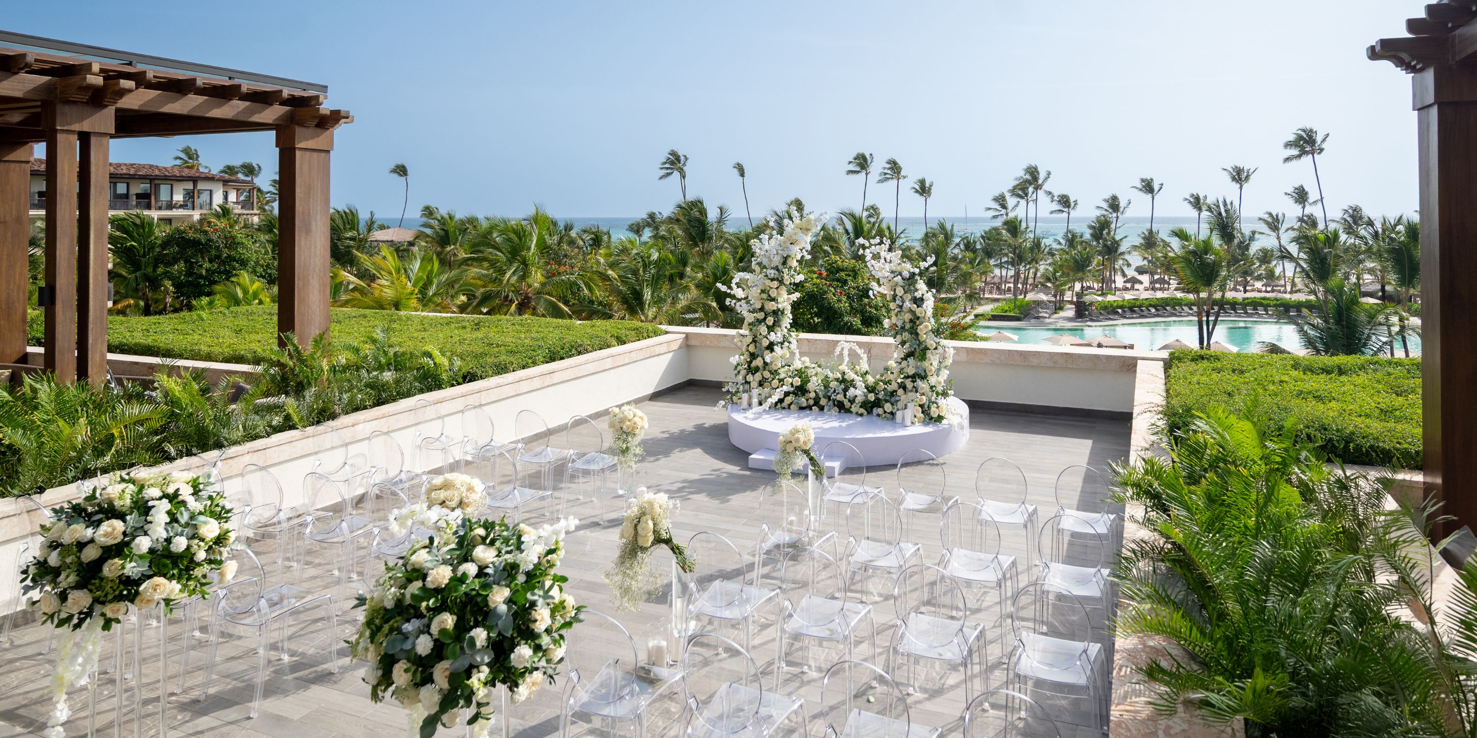 Destination wedding setup at Lopesan Costa Bavaro featuring white florals, clear chairs, and palm trees.