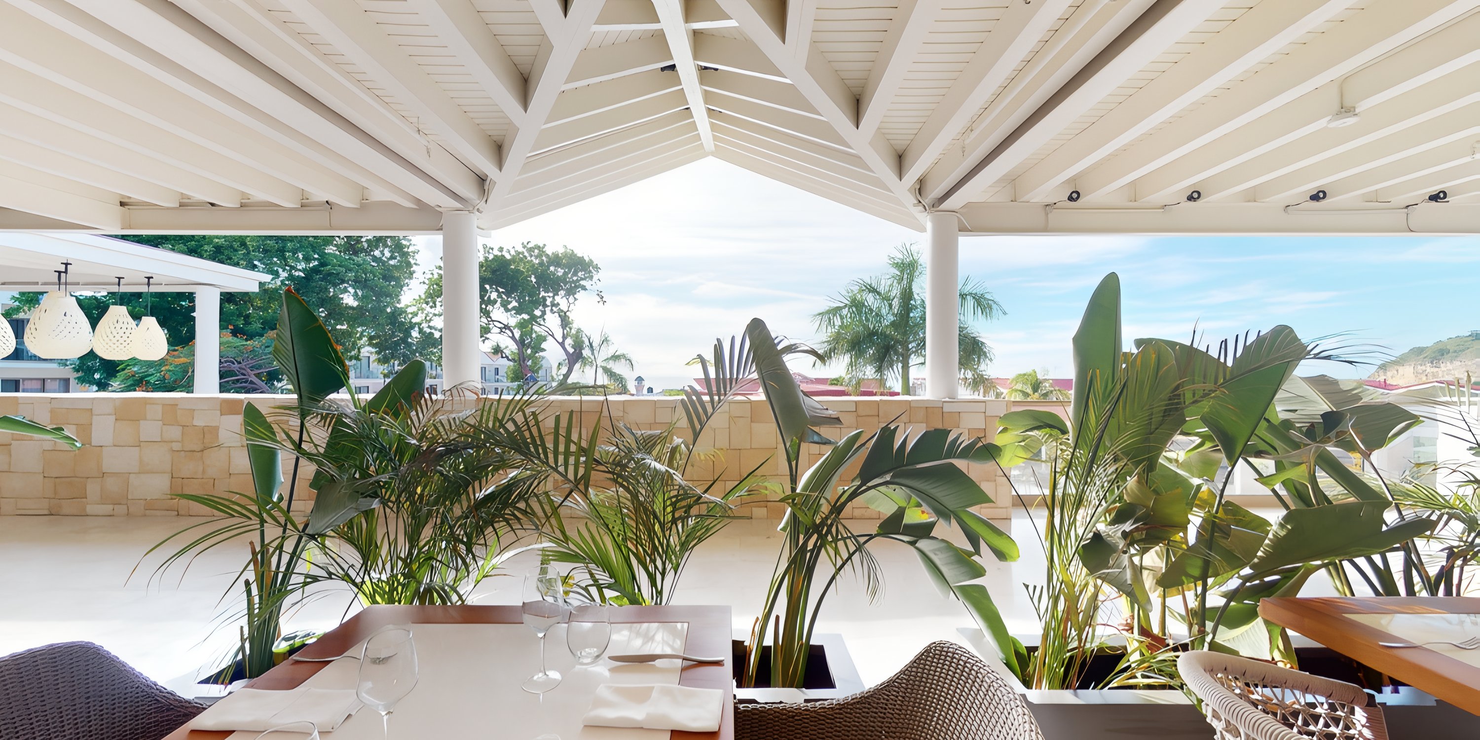 Royalton Chic Antigua: Patio with wooden roof, tropical plants, and set tables for a destination wedding.