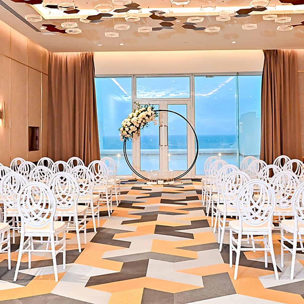 Rows of white chairs face a circular floral arch at a destination wedding by the ocean.