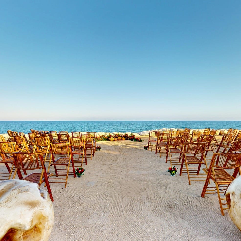 Rows of wooden chairs arranged for a beach destination wedding facing the ocean.