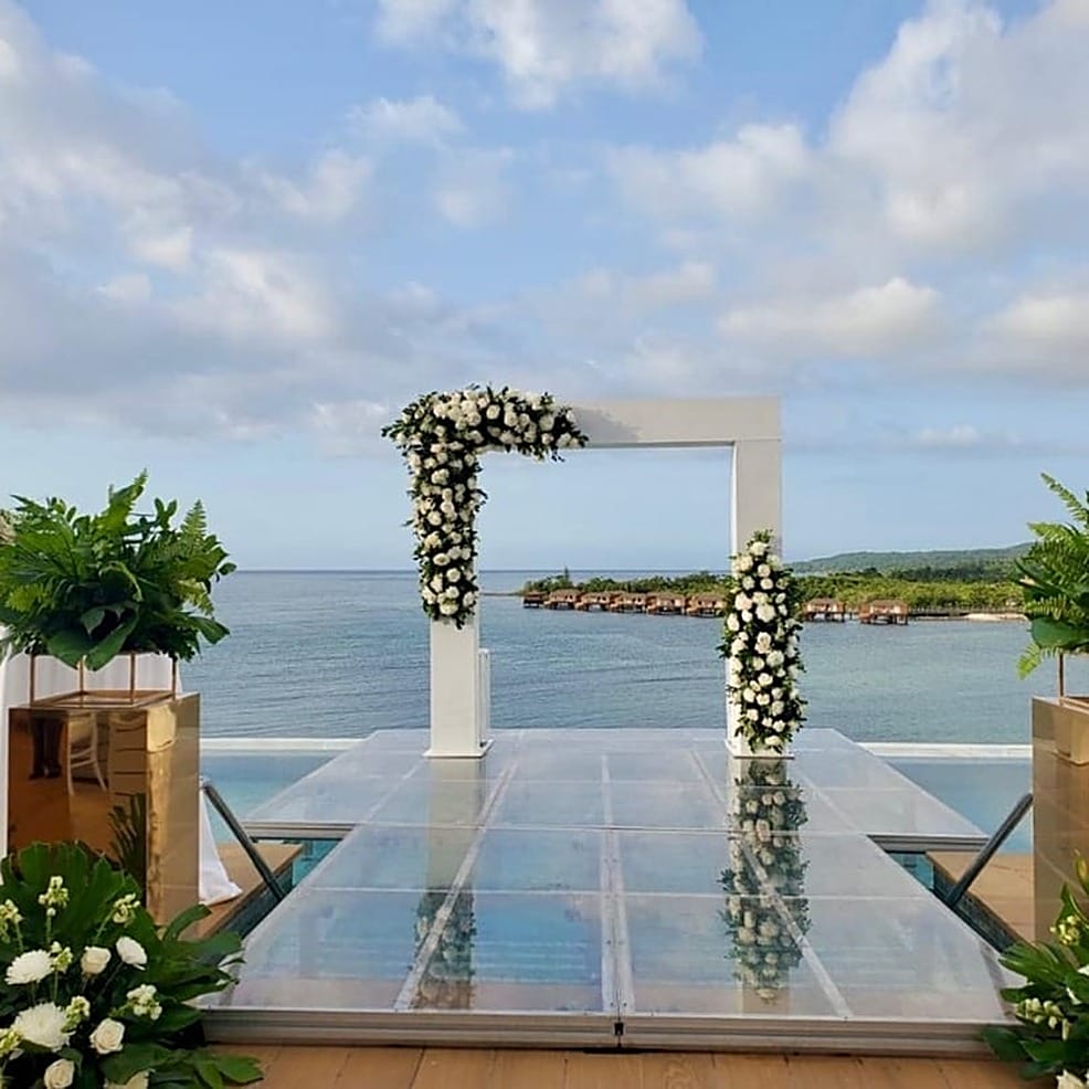 Floral wedding arch on a glass platform overlooking the ocean at a destination wedding.