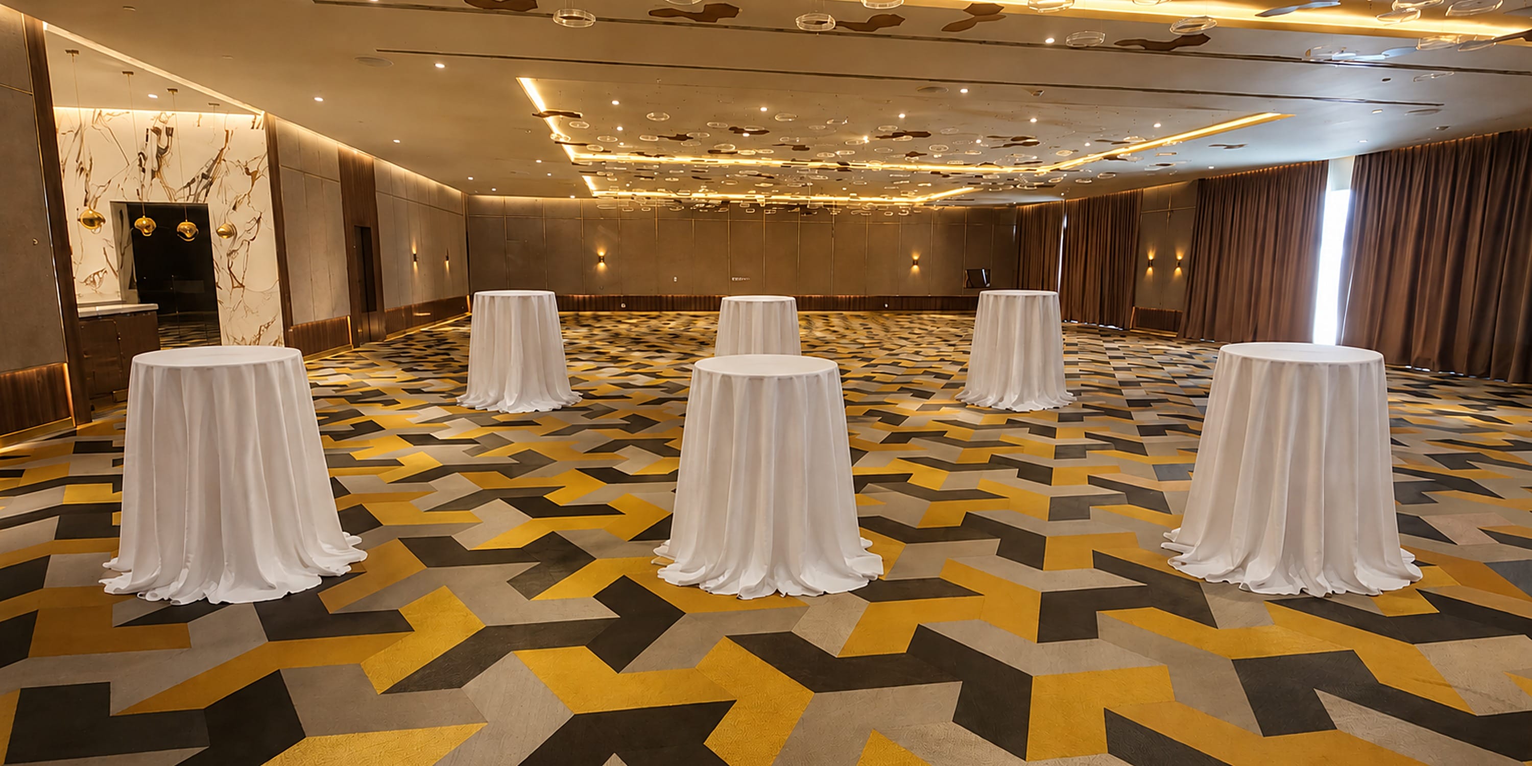 Five white-clothed high-top tables in a Princess Grand Jamaica wedding banquet hall.