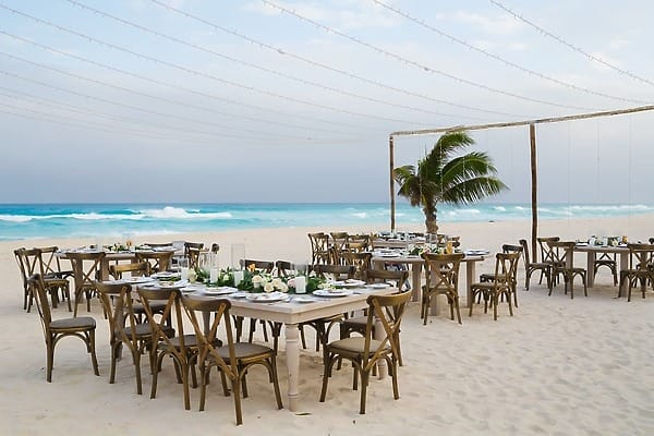 Tables set for a destination wedding on the sand at Wyndham Grand Cancun, with waves and palm tree.