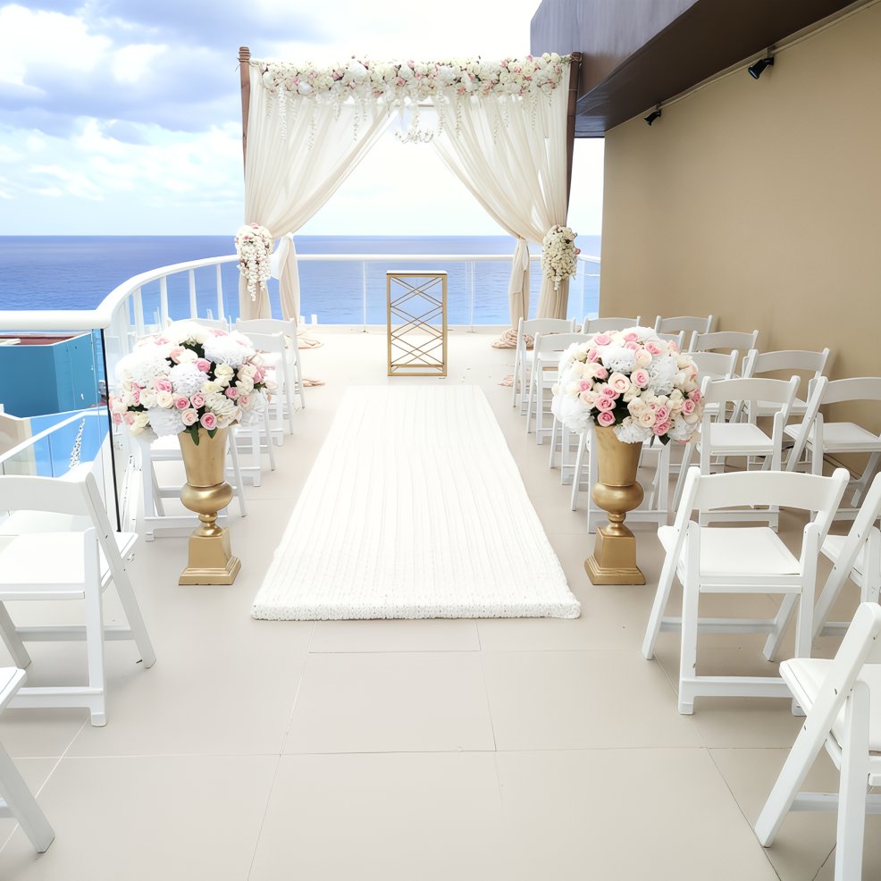 Destination wedding setup outdoors with rows of white chairs, floral decor, and a stunning ocean view.