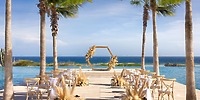 Destination wedding ceremony at Secrets Baby Beach Aruba with wooden chairs and a hexagonal arch on the oceanfront.