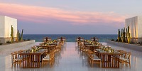 Oceanview outdoor dining with wooden tables and chairs at sunset, perfect for a destination wedding.
