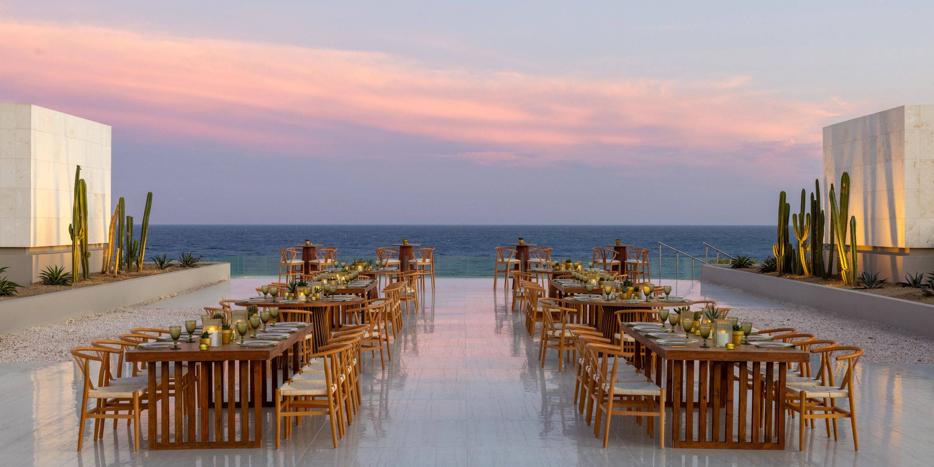 Oceanview outdoor dining with wooden tables and chairs at sunset, perfect for a destination wedding.
