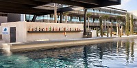 Poolside bar at Secrets Baby Beach Aruba, ideal for destination wedding; liquor bottles, modern building.