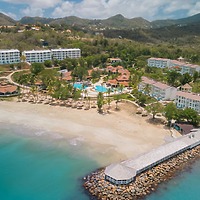 Secrets St Lucia: a beachfront destination wedding resort with pools, palm trees, and hills below clouds.
