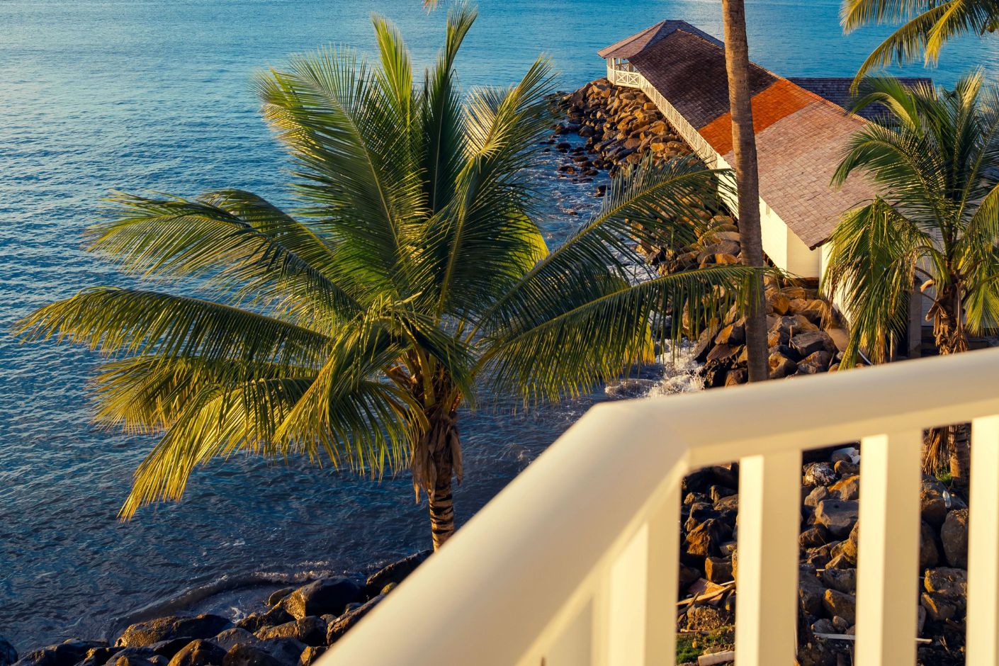 Balcony view at Secrets St Lucia: palm trees, rocky shore, and oceanfront destination wedding venue.