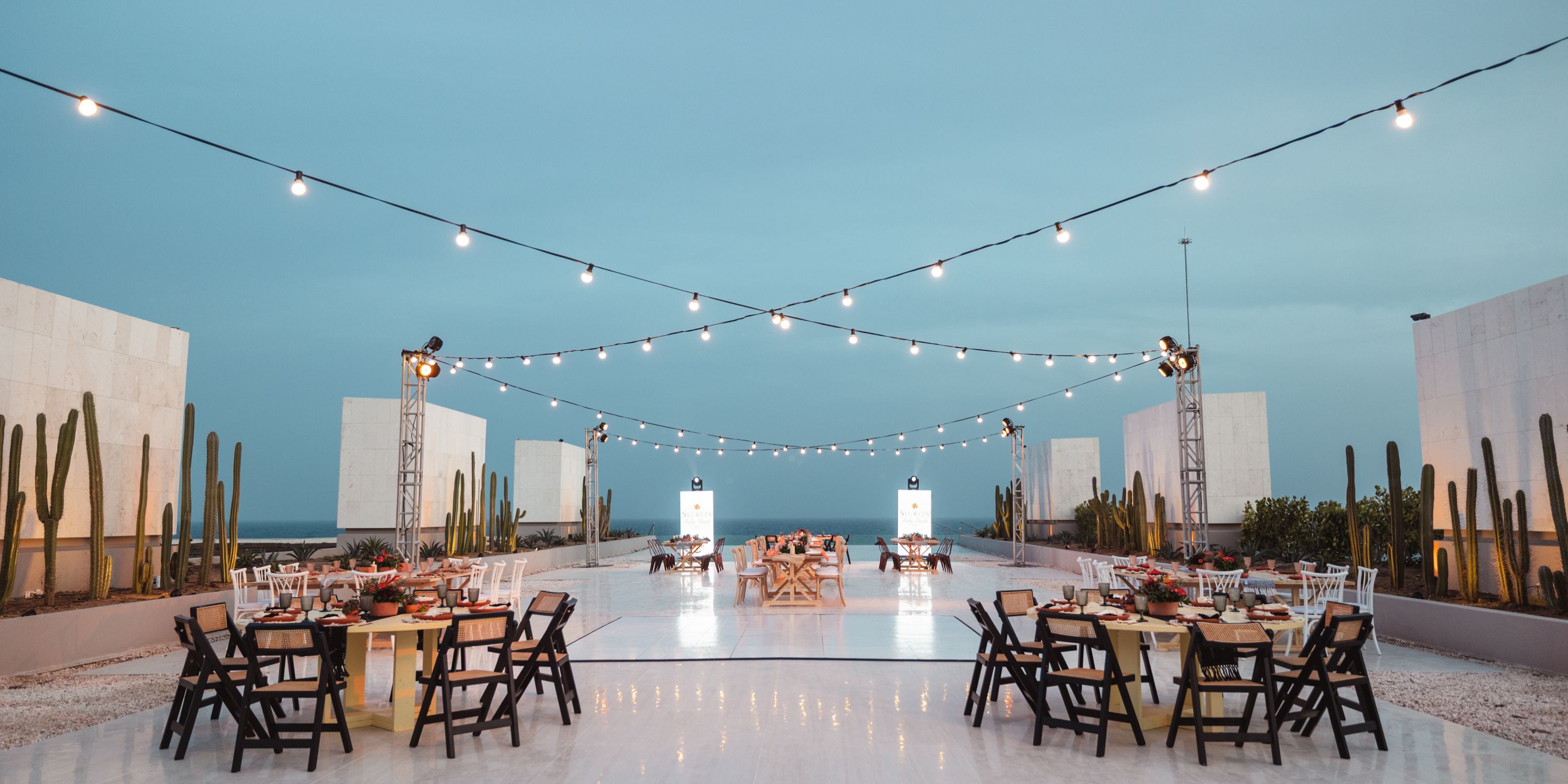 Rooftop destination wedding space at Secrets Baby Beach Aruba with string lights, round tables, and cacti.
