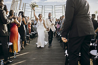Carina and Marvin walk hand in hand down the aisle at their destination wedding as guests applaud.