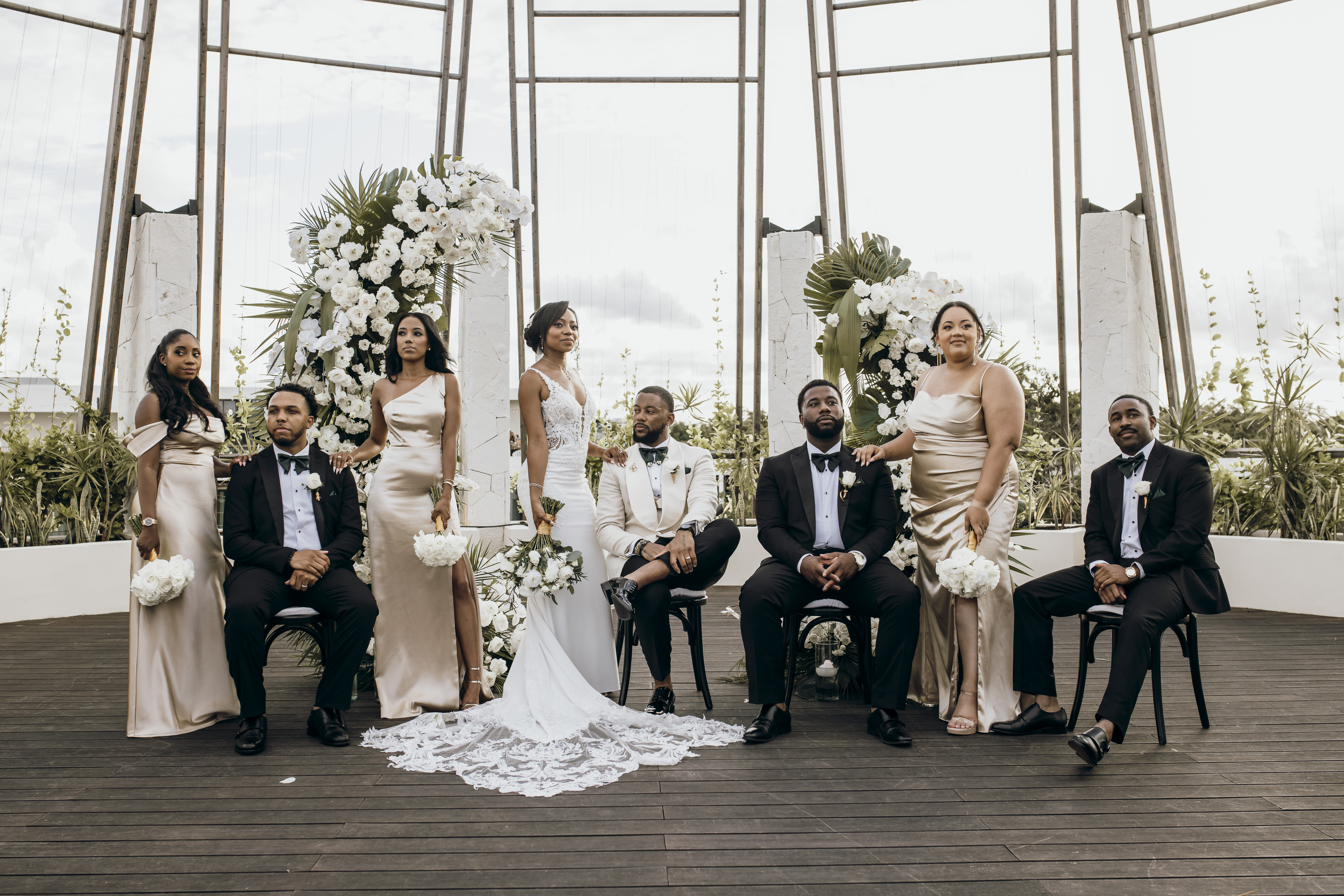 Carina and Marvin pose at the center indoors during their wedding, surrounded by bridesmaids and groomsmen.