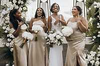Four women in formal dresses show Carina and Marvin rings at a destination wedding, holding white bouquets.