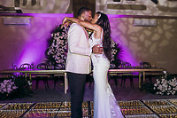 Carina and Marvin share a kiss at their destination wedding on a floral dance floor with purple lighting.
