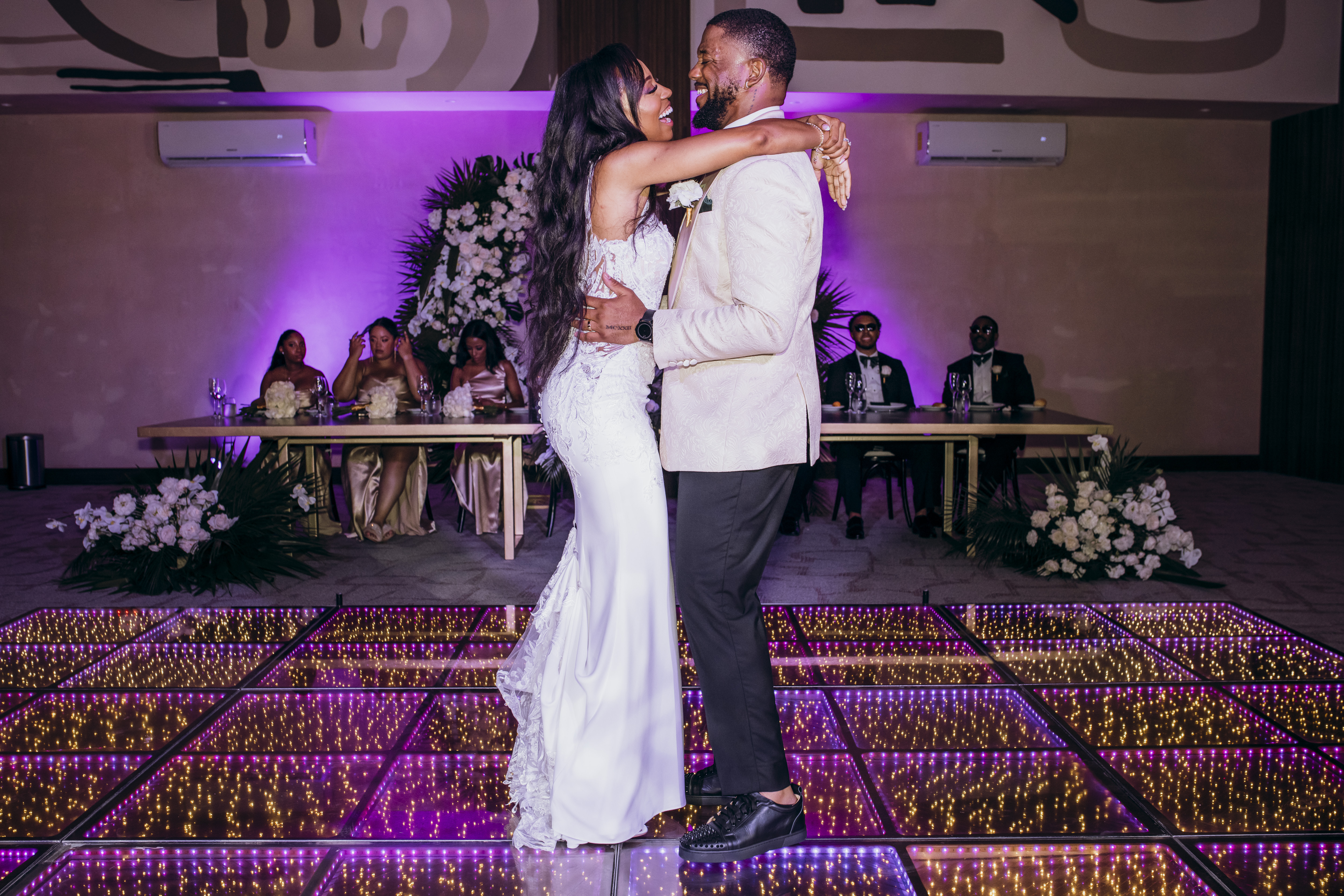 Carina and Marvin dance on a glowing floor at a destination wedding, guests seated behind them.