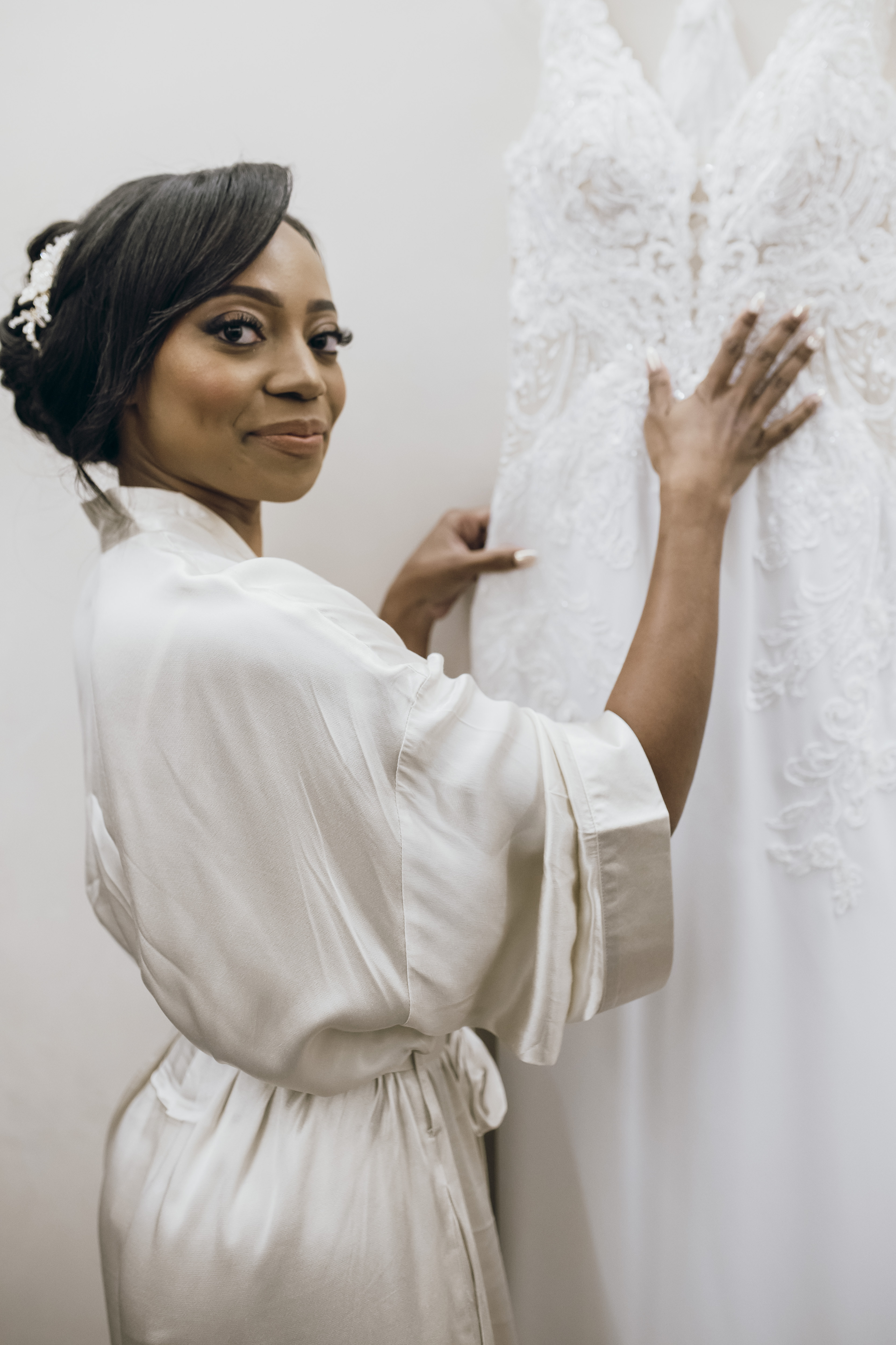 Woman in white robe touches Carina and Marvin lace wedding dress on hanger before destination wedding.