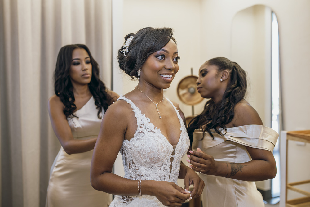 Bride in white lace with two bridesmaids in cream dresses preparing for the wedding ceremony.
