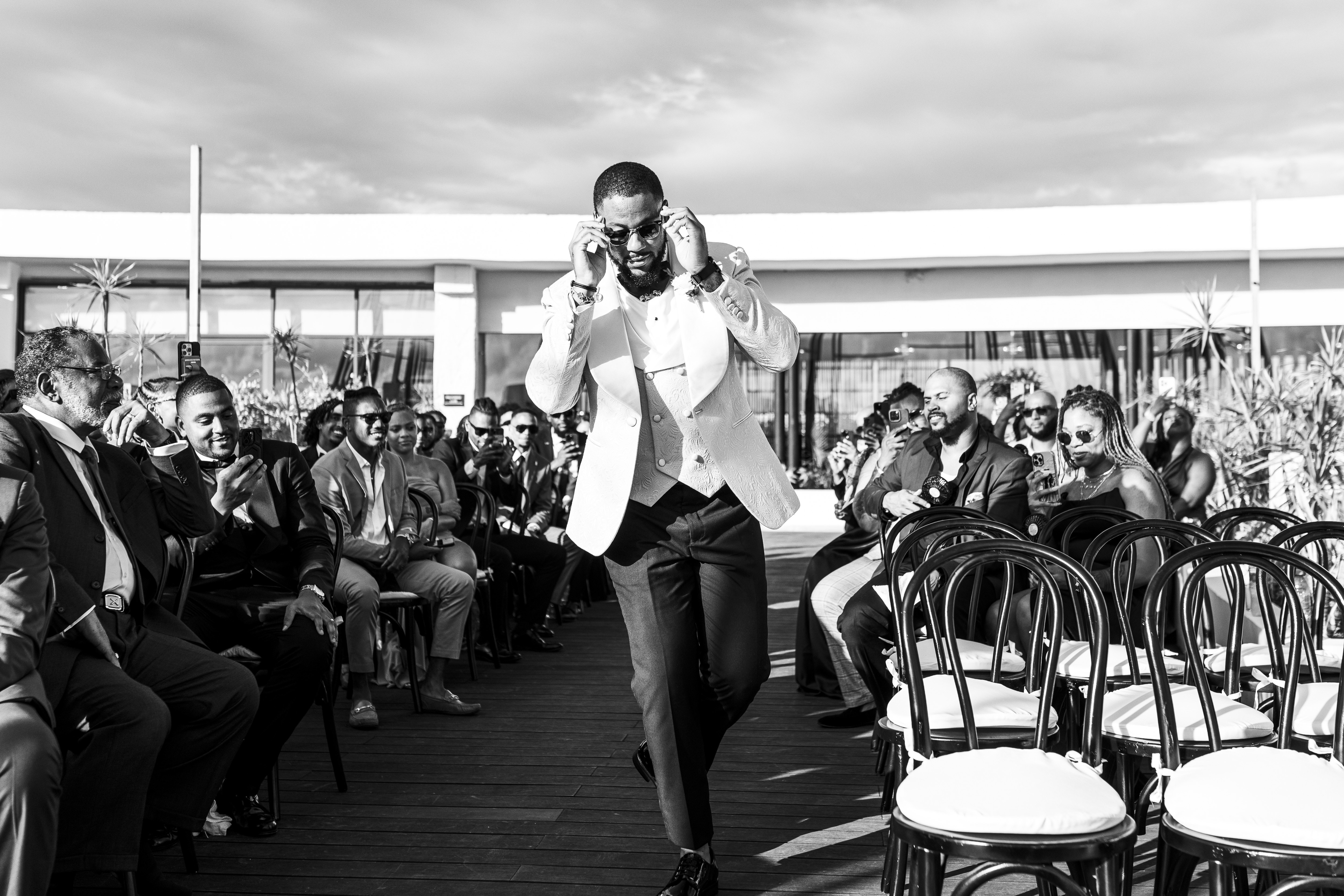 Carina and Marvin walk down the aisle at their destination wedding, as smiling guests look on outdoors.