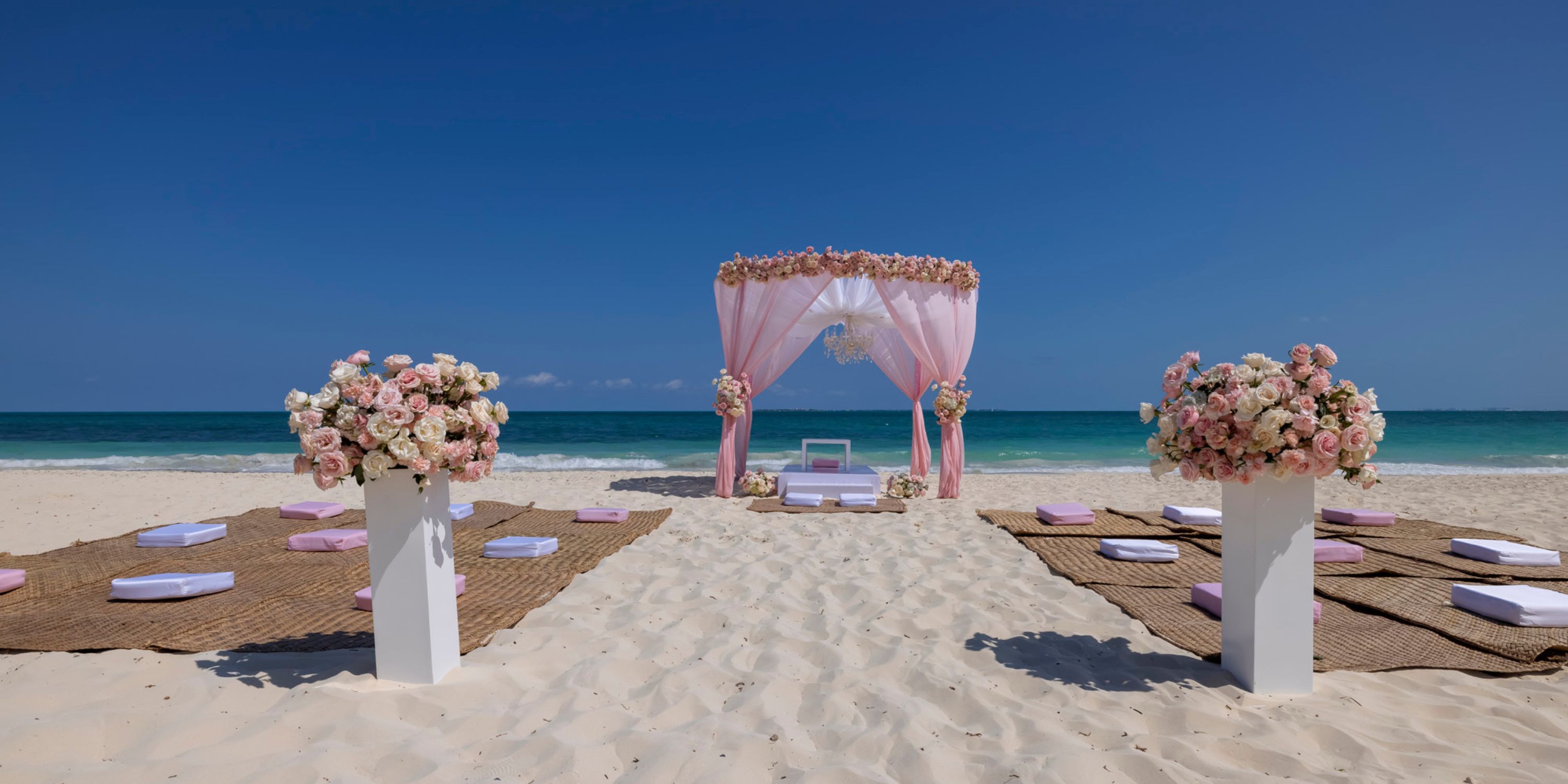 Destination wedding altar on the beach adorned with pink flowers at Planet Hollywood Adult Scene Cancun.
