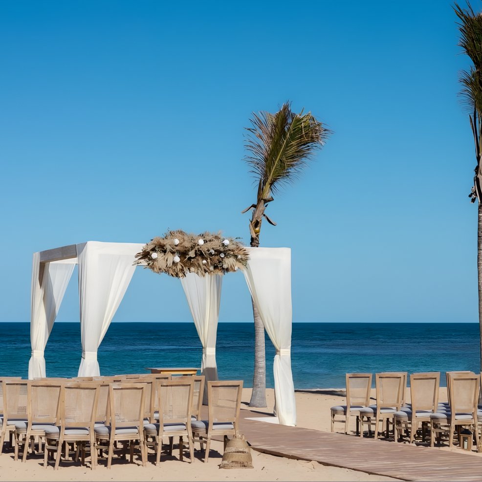Wooden chairs and a white canopy arranged for a destination wedding on the beach beneath blue skies.