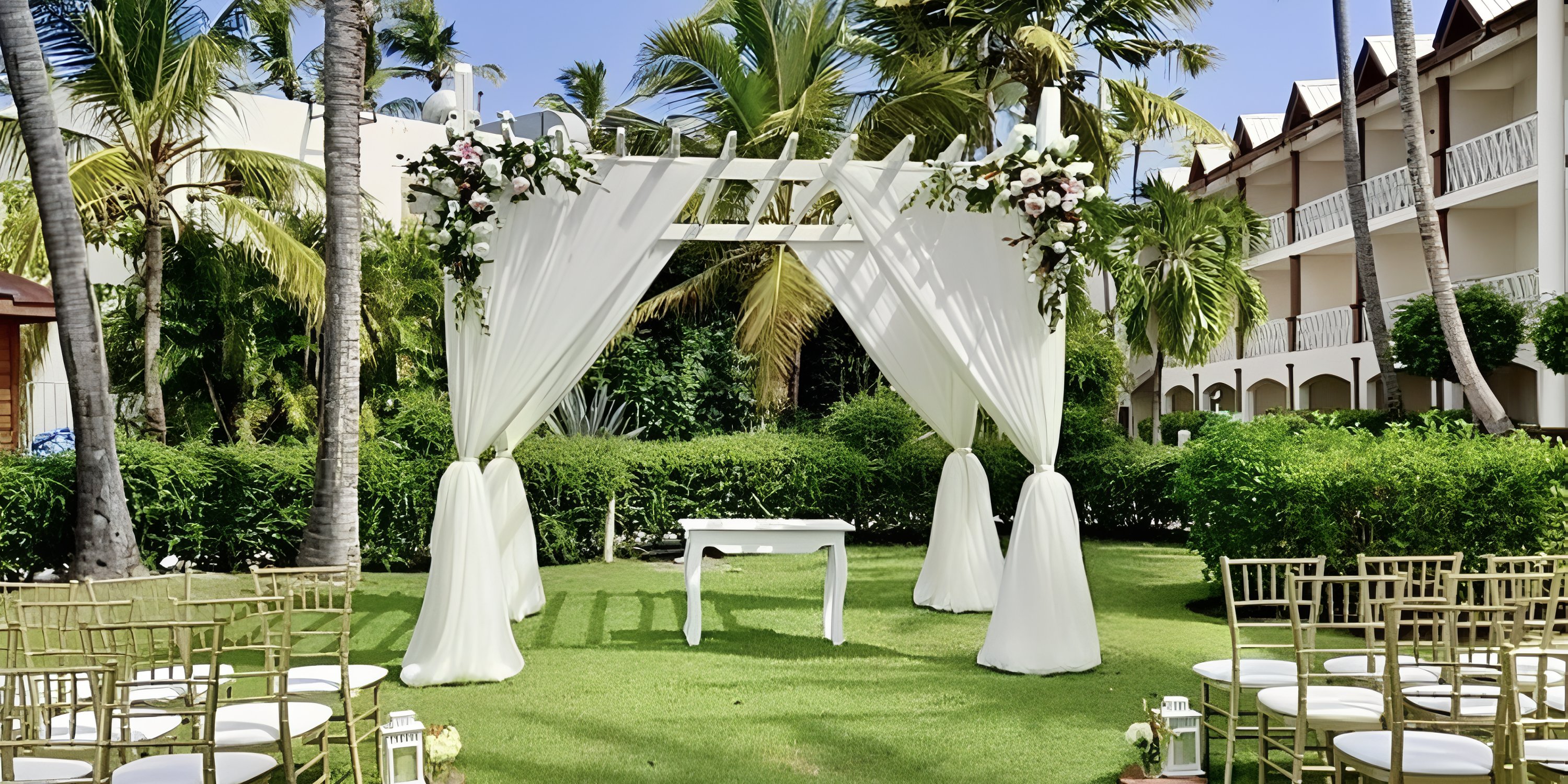 A destination wedding setup on a lawn at Sunscape Coco Punta Cana with white drapes, flowers, and chairs.