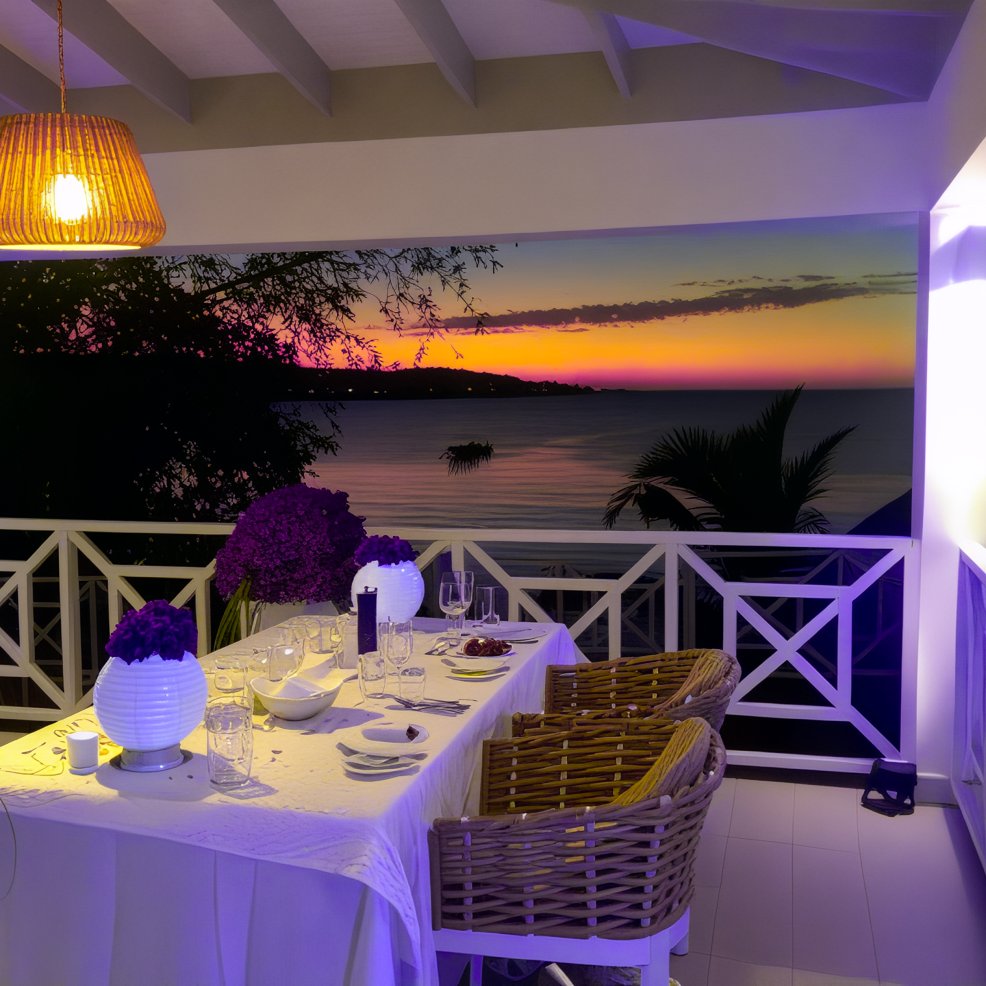 A dinner table is set for a destination wedding on a balcony overlooking the ocean at sunset.