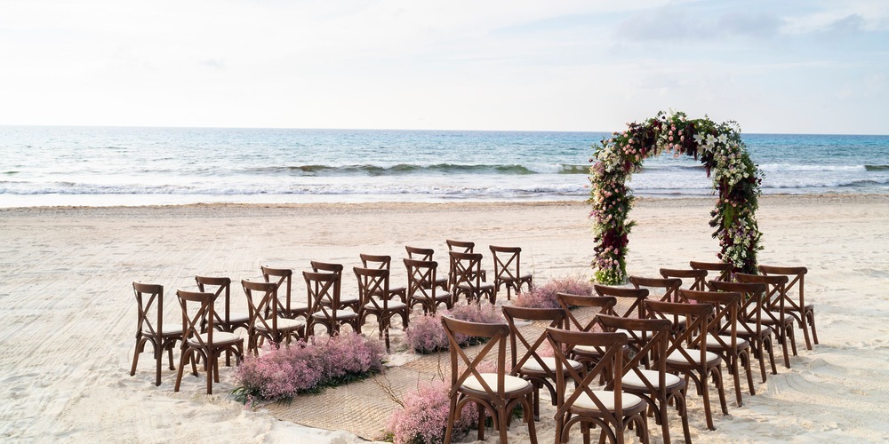 Rows of chairs and a floral arch prepared for a destination wedding ceremony for 50 guests on the beach.