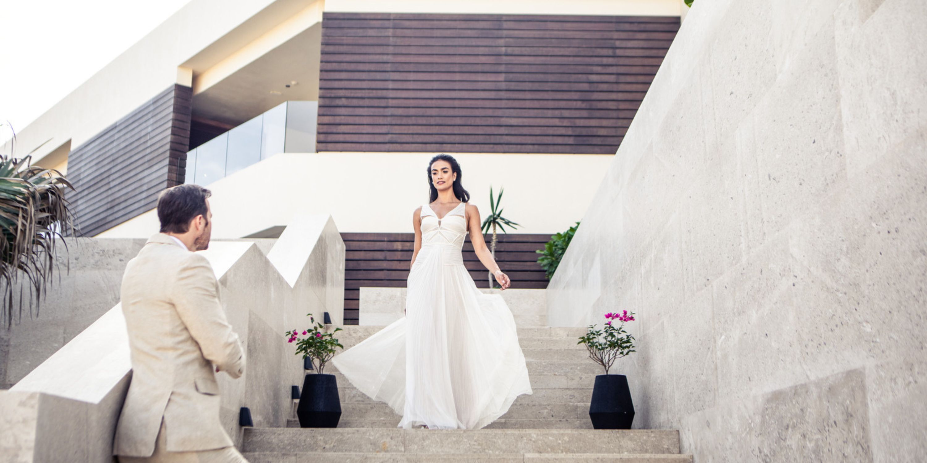 Bride in white dress descends Nobu Hotel Los Cabos stairs toward groom at destination wedding.