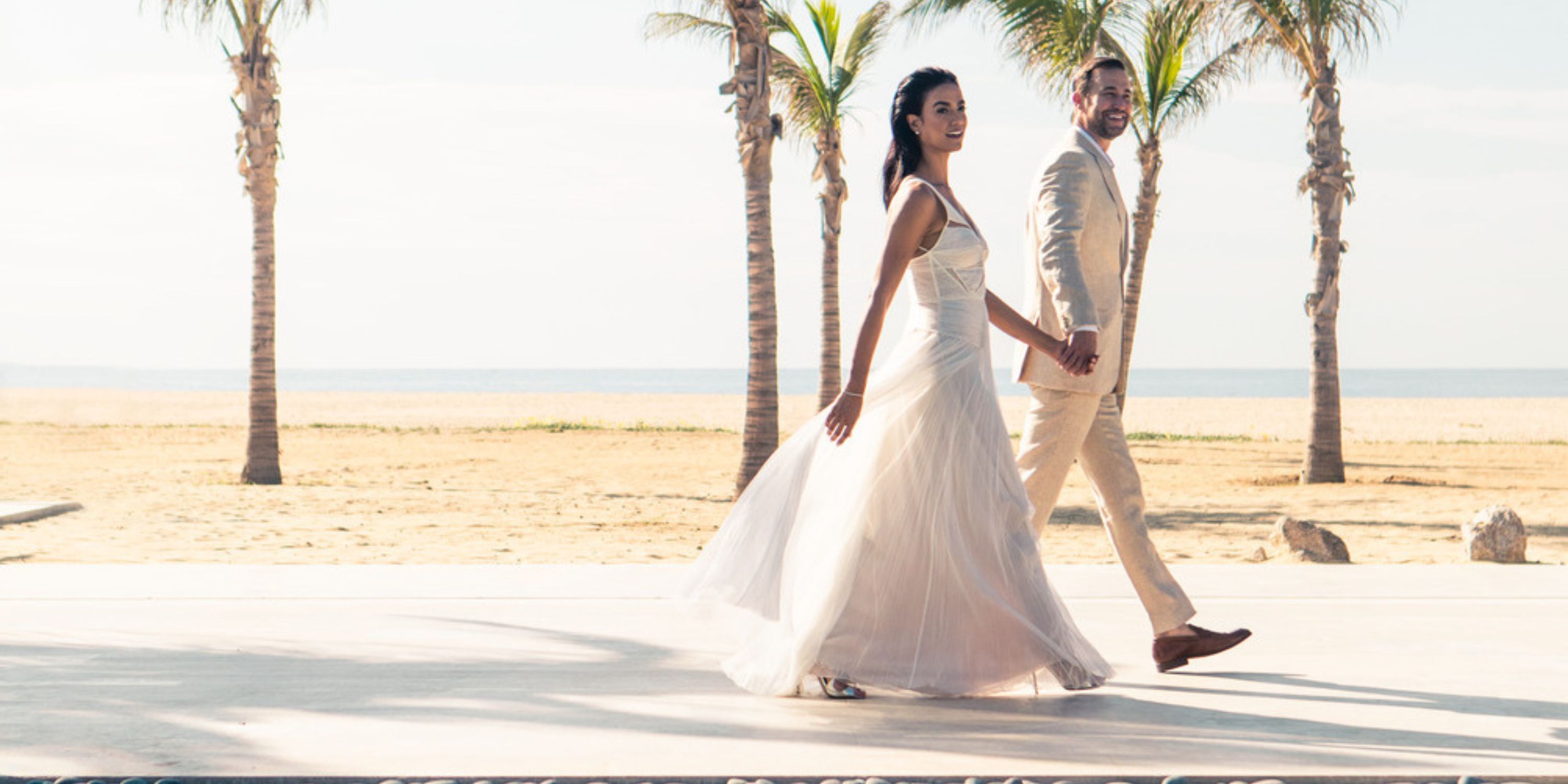 Bride and groom hold hands by palm trees during their destination wedding at Nobu Hotel Los Cabos.