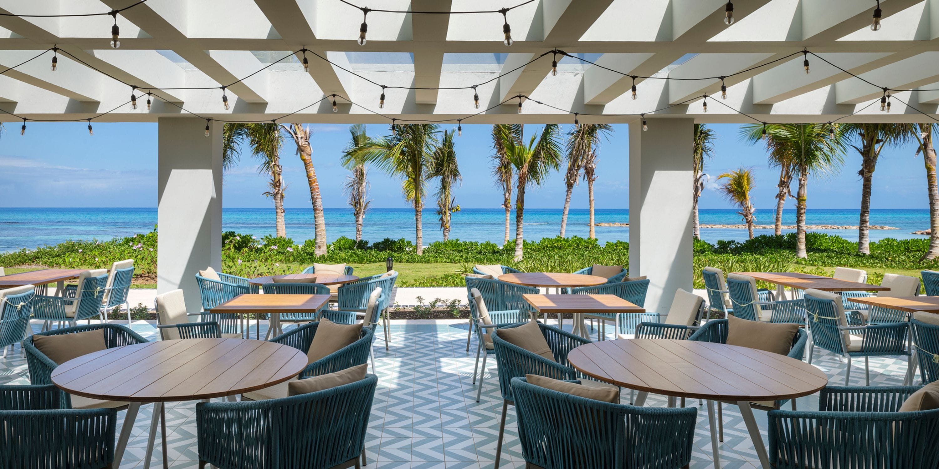 Ocean Eden Bay patio set for a destination wedding, round tables, blue chairs, and ocean views framed by palms.