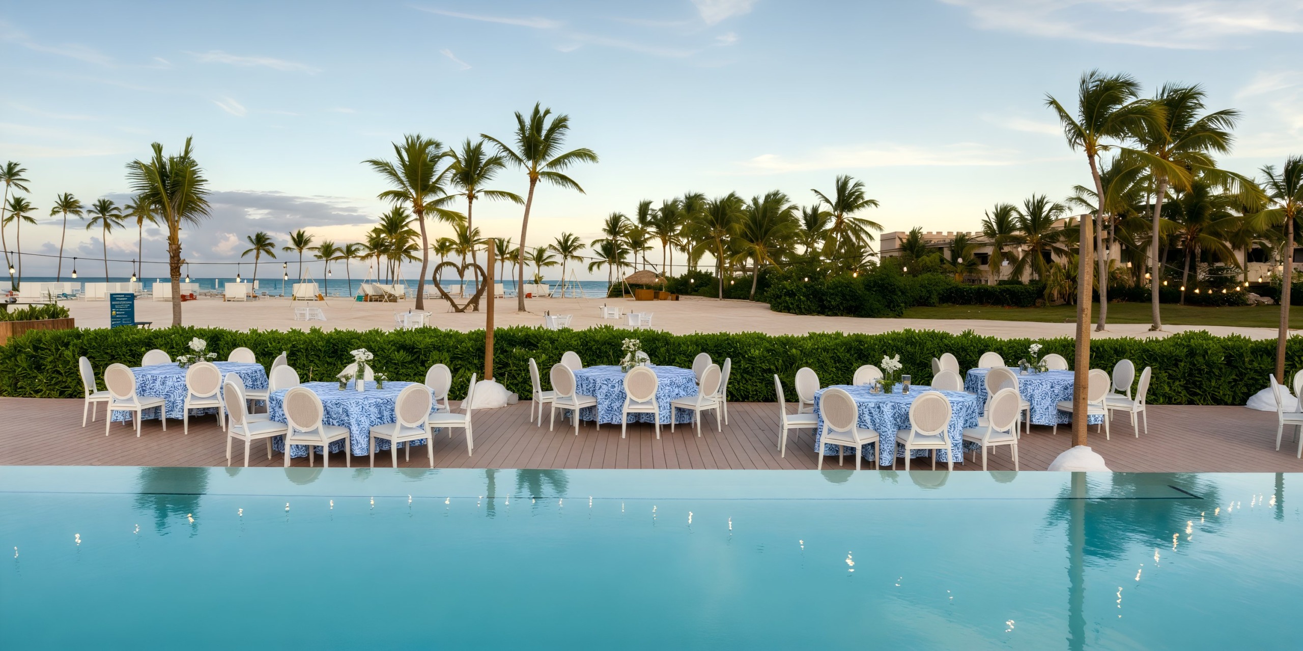 Enjoy outdoor dining at Dreams Cap Cana Resort & Spa, nestled by a picturesque pool surrounded by swaying palm trees and offering a breathtaking beach view—an ideal setting for a destination wedding celebration.
