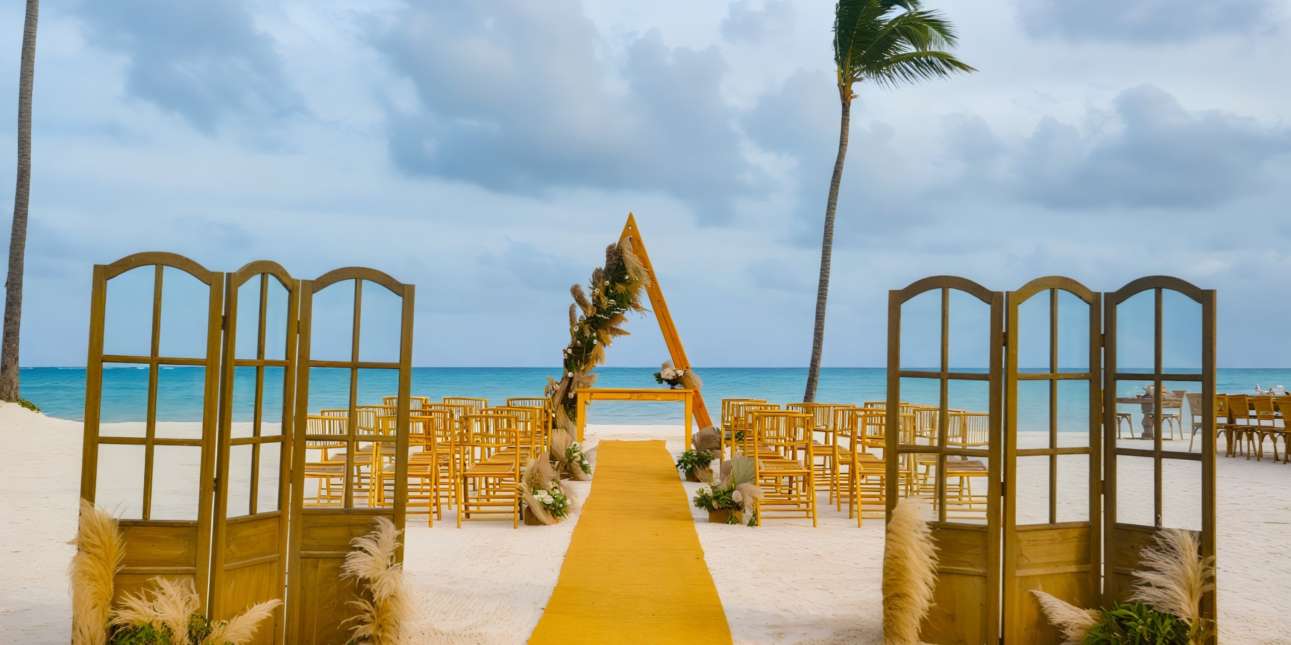 A destination wedding setup at Dreams Cap Cana features a stunning beachfront arrangement with wooden chairs and a triangular arch facing the ocean.