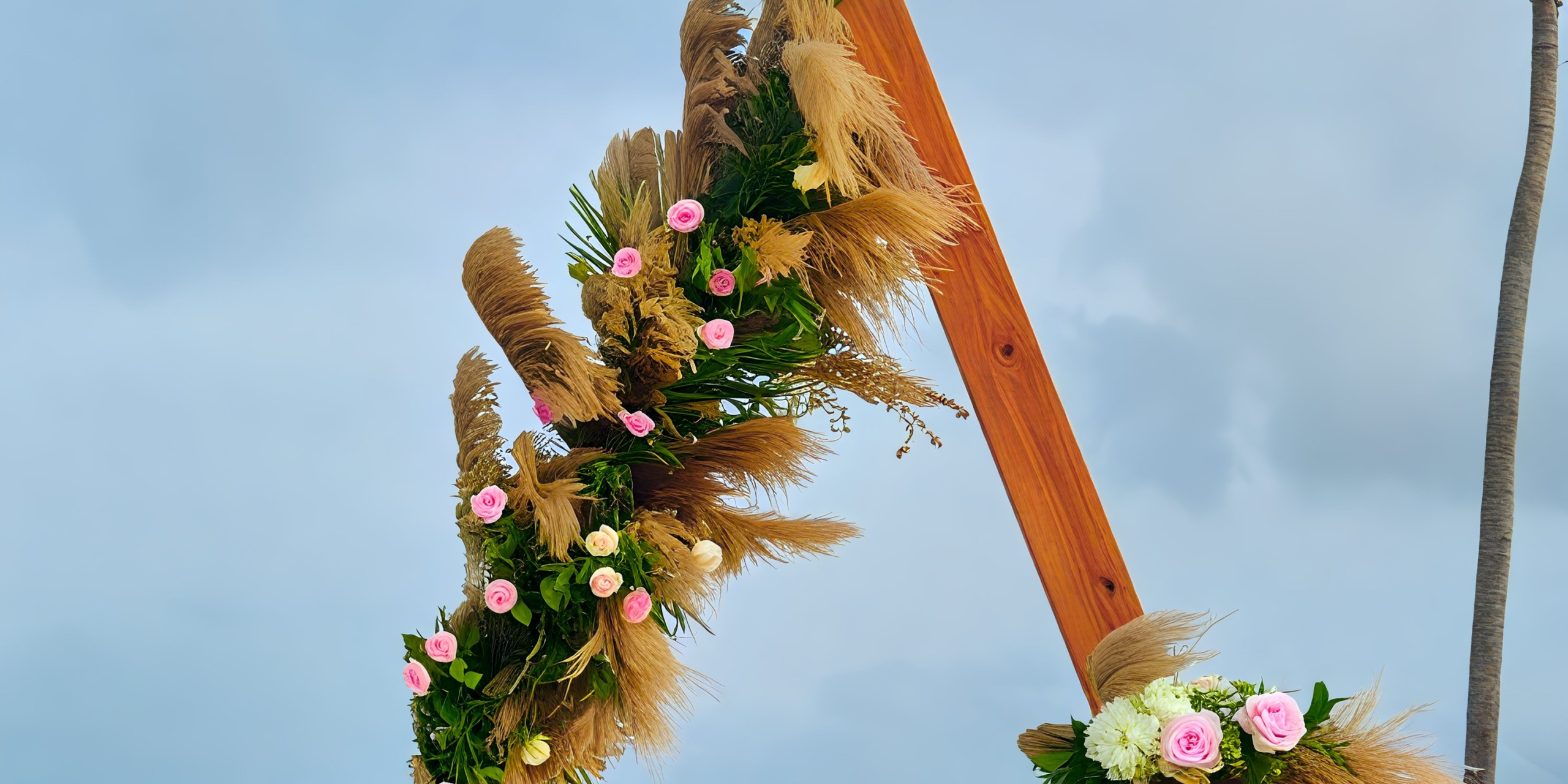 A beautifully adorned arch with vibrant flowers and lush grass stands ready for a destination wedding at Dreams Cap Cana, set against the backdrop of a cloudy sky.