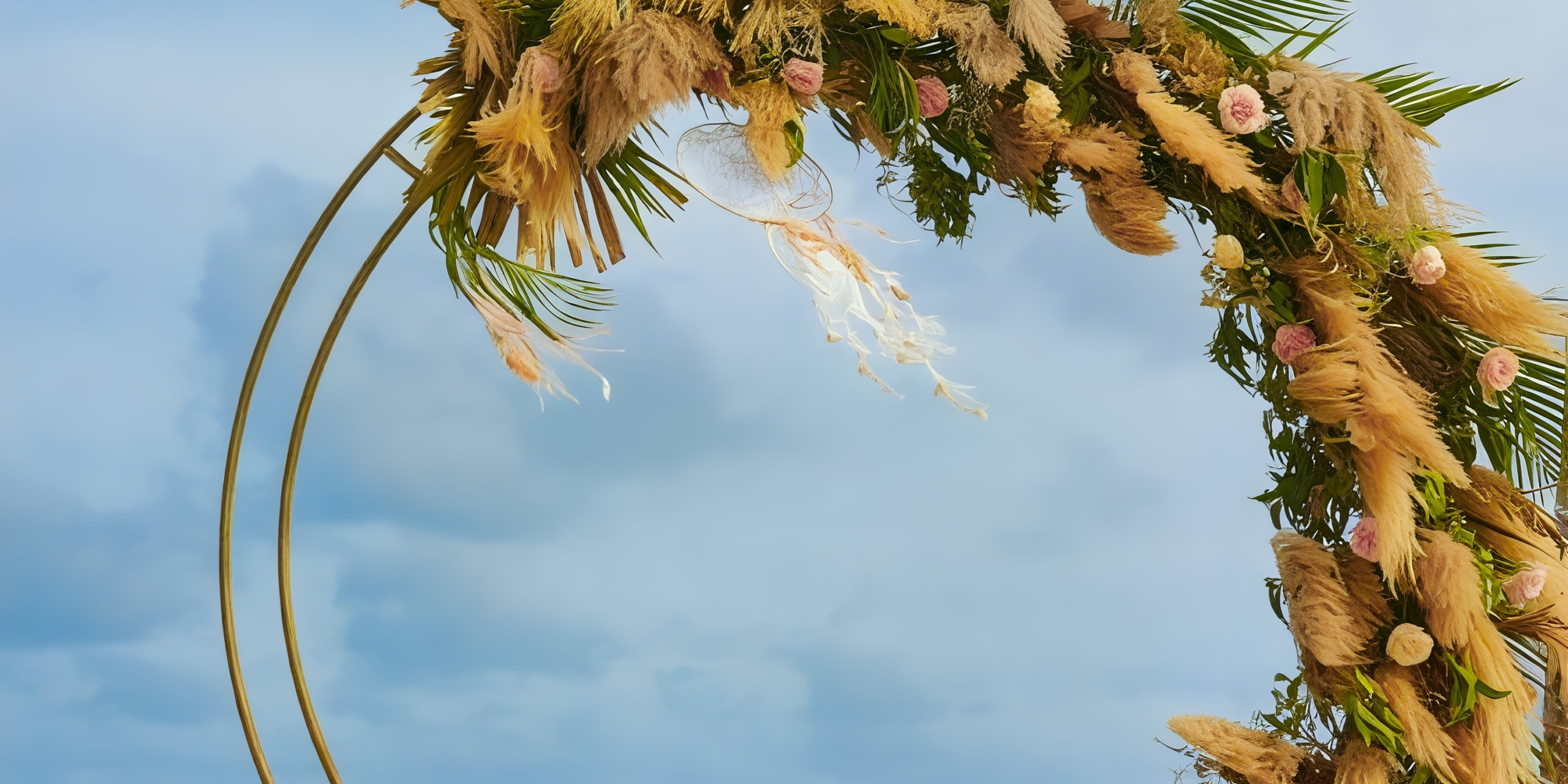 A floral arch graces Dreams Cap Cana Resort & Spa, creating a picturesque setting for a destination wedding beneath the cloudy blue sky.