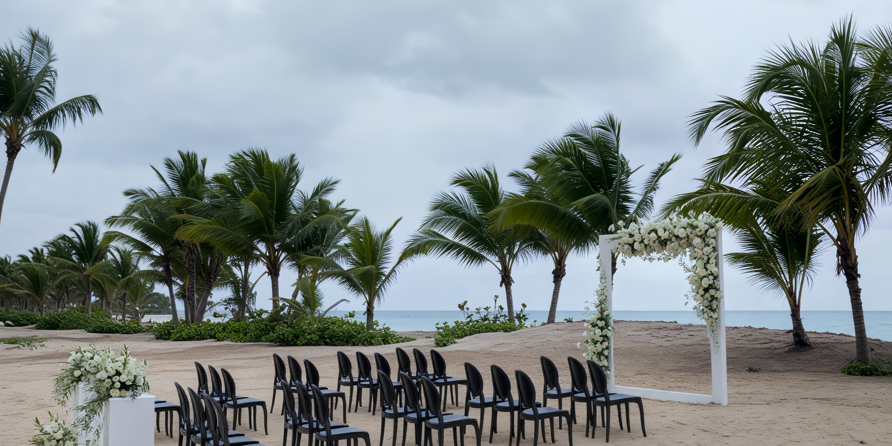 Black chairs and a floral arch arranged for a destination wedding at Dreams Playa Esmeralda on a cloudy beach.