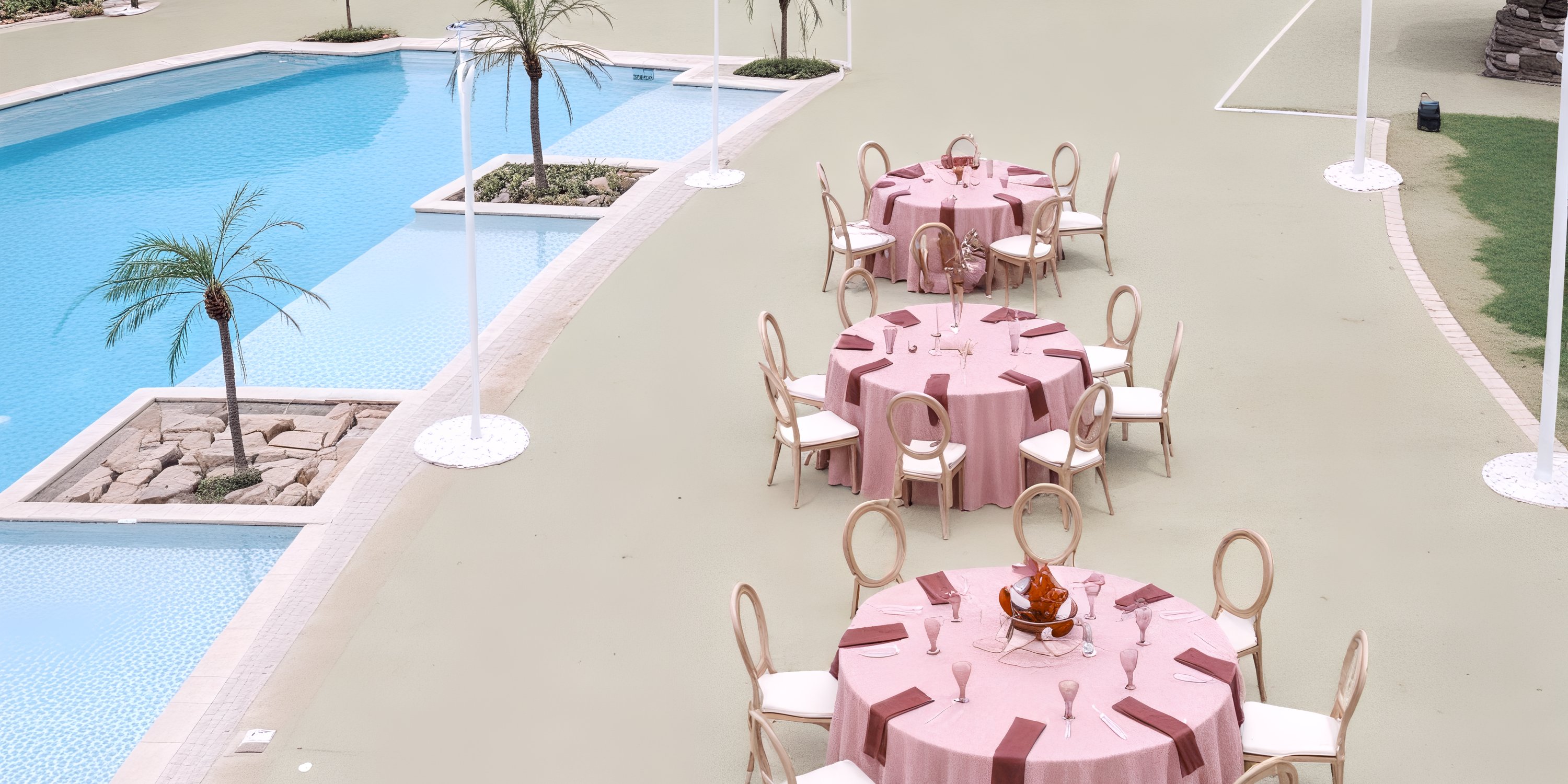 Round tables with pink cloths and chairs set up for a destination wedding by the pool at Dreams Playa Esmeralda.