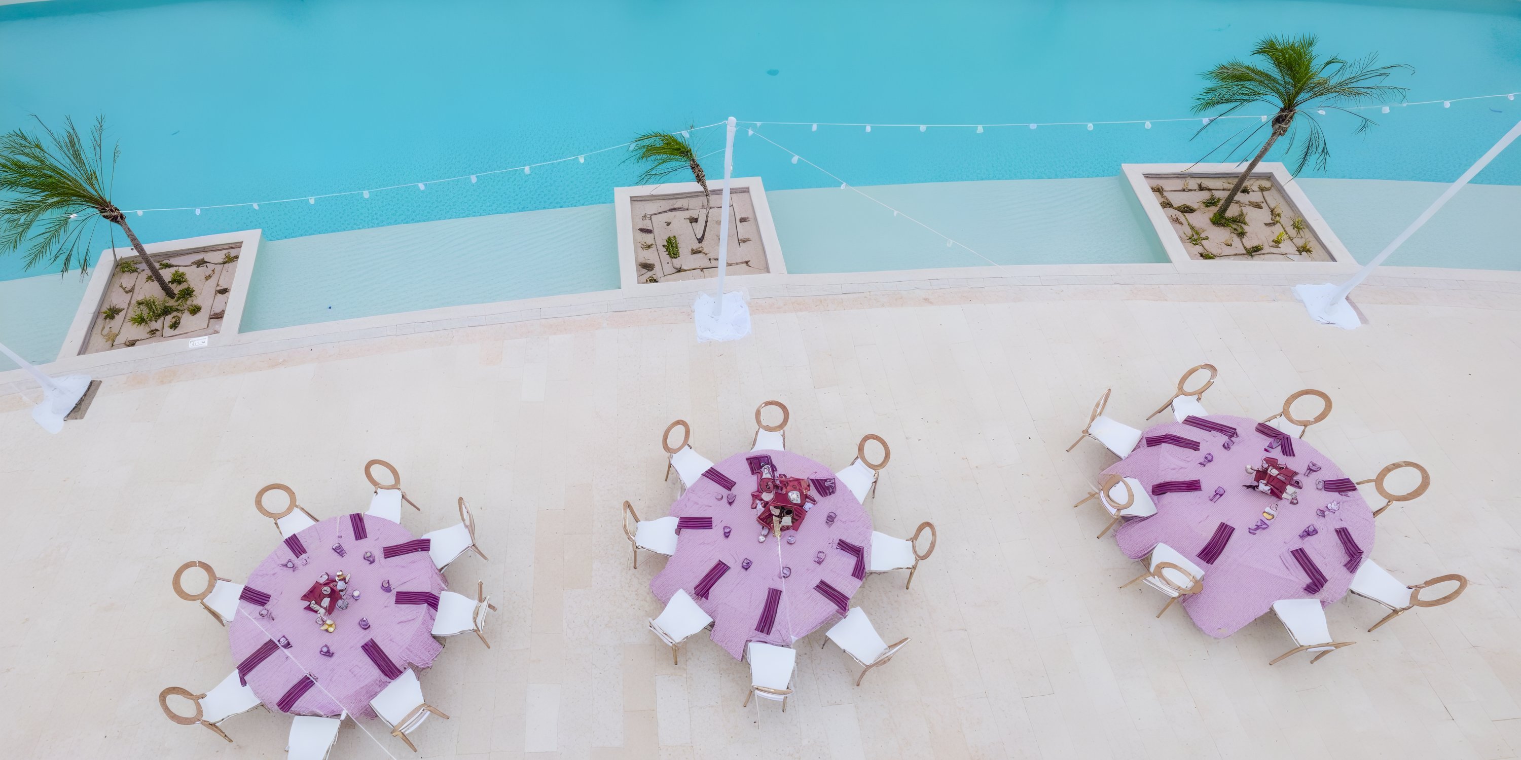 Three round tables with purple cloths and chairs set up for a destination wedding by the pool.