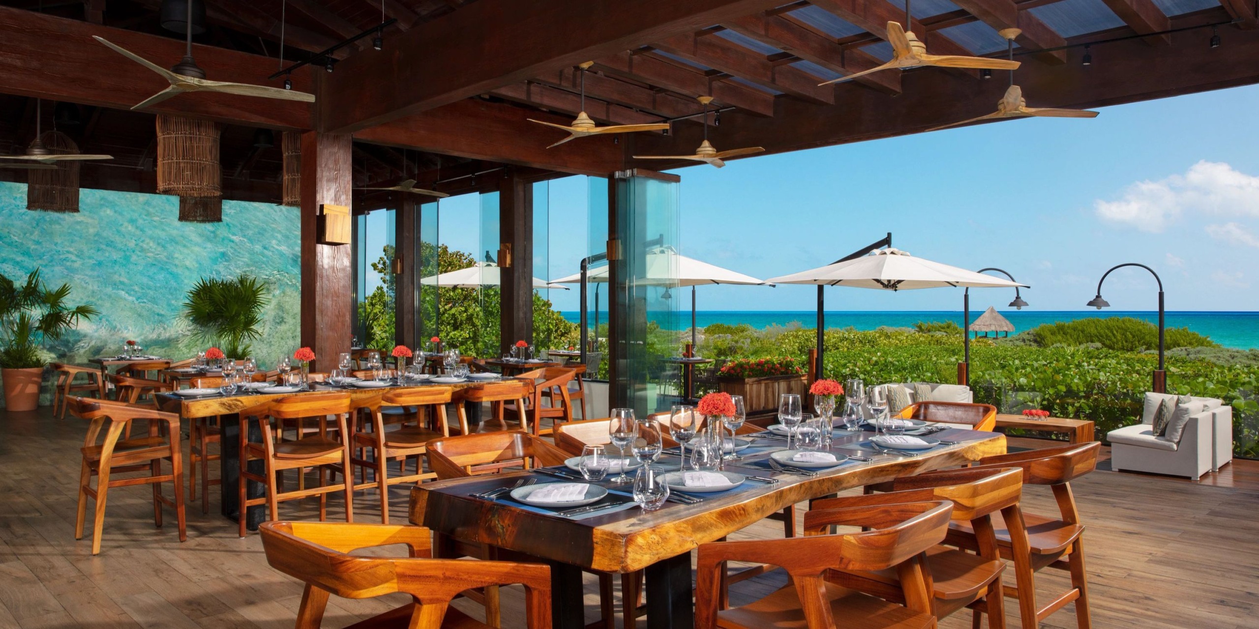 An open-air restaurant with wooden tables and chairs, offering a stunning backdrop of the ocean—perfect for a destination wedding.
