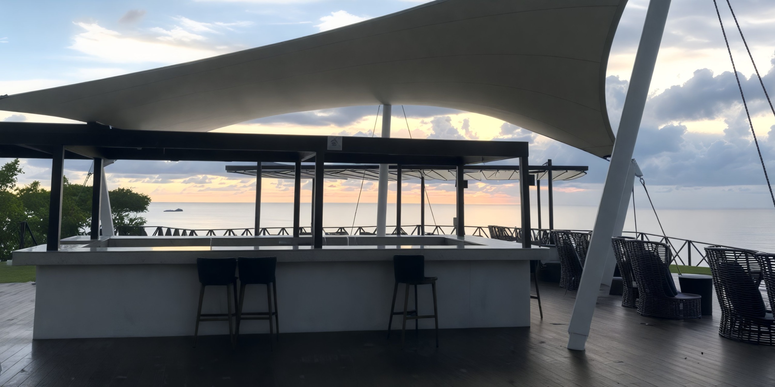 A chic outdoor bar with a contemporary canopy provides a perfect setting for a destination wedding, offering breathtaking views of the ocean as the sun sets.