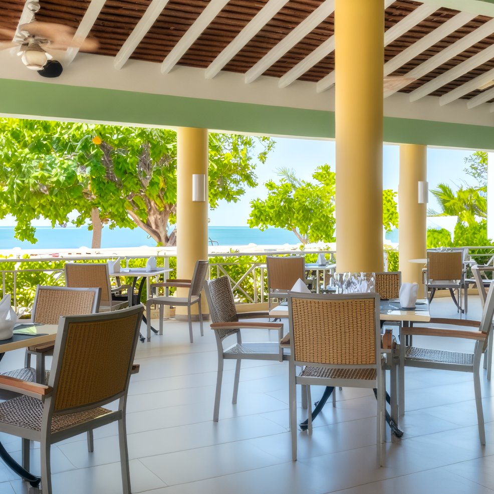 Outdoor restaurant patio set for a destination wedding, with empty tables, chairs, trees, and ocean views.