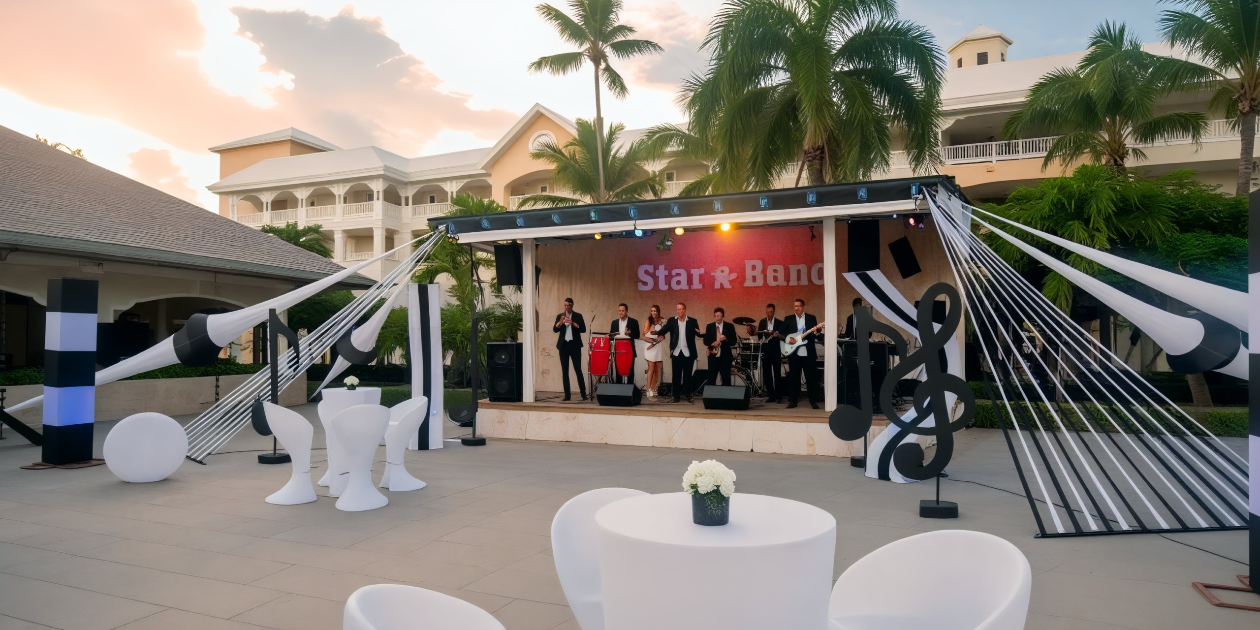 An outdoor stage hosts a live band performance, surrounded by tables and palm trees, creating the perfect ambiance for a destination wedding.