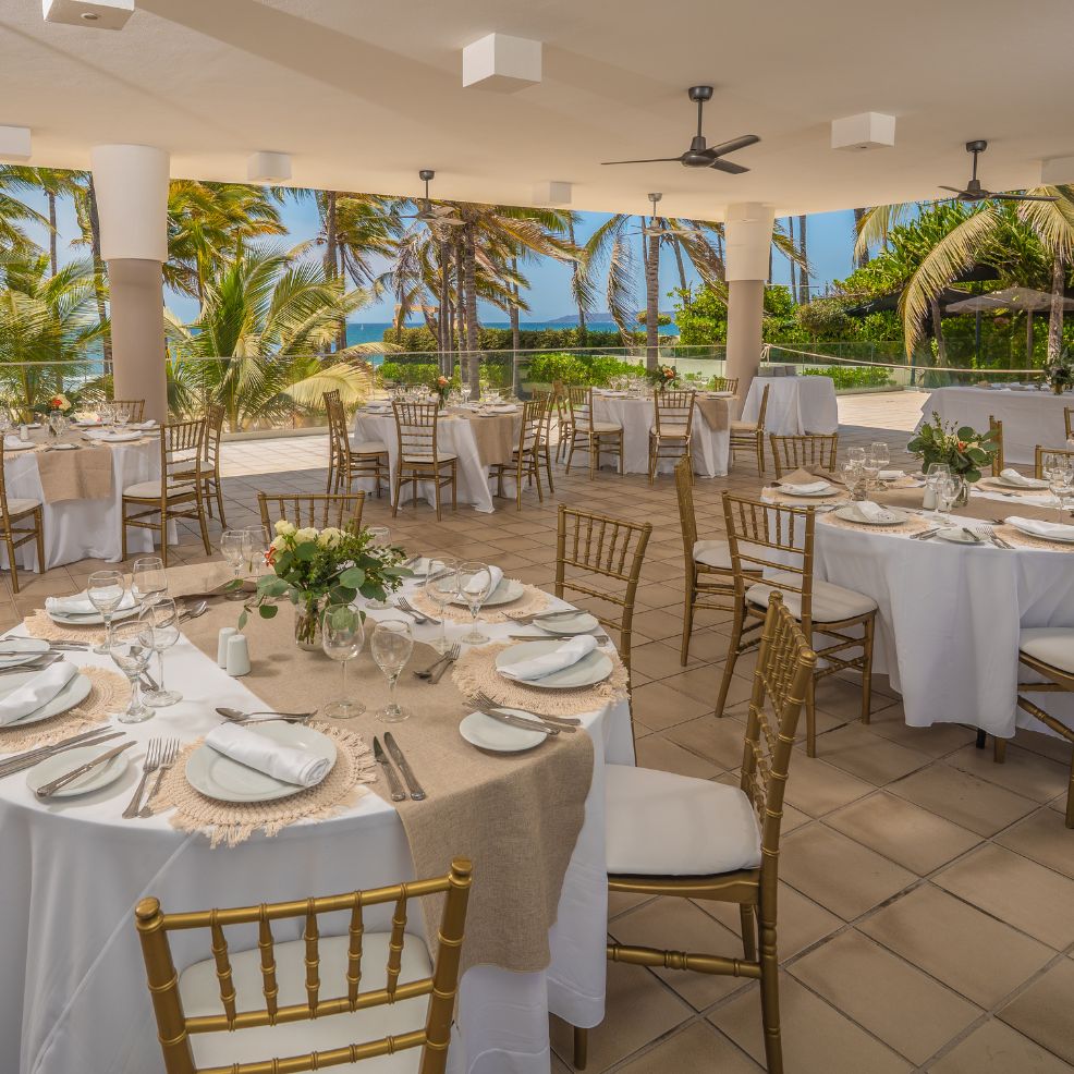Destination wedding setup with round tables, white linens, gold chairs, and lush tropical scenery.