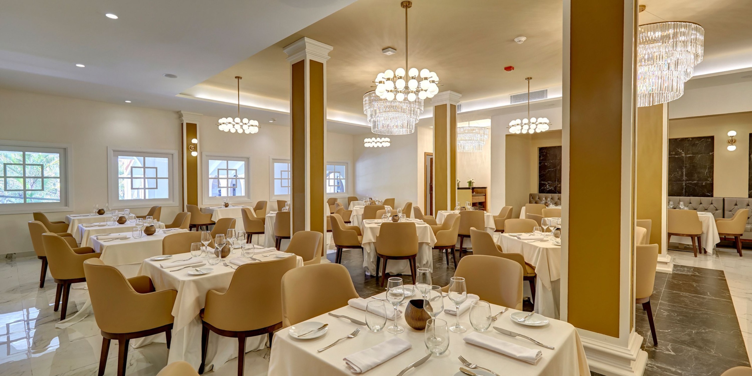 The restaurant's elegant interior, featuring beige chairs and tables adorned with white tablecloths, creates a perfect setting for a destination wedding. Chandeliers add a touch of sophistication to the ambiance, making it an ideal venue for your special day.