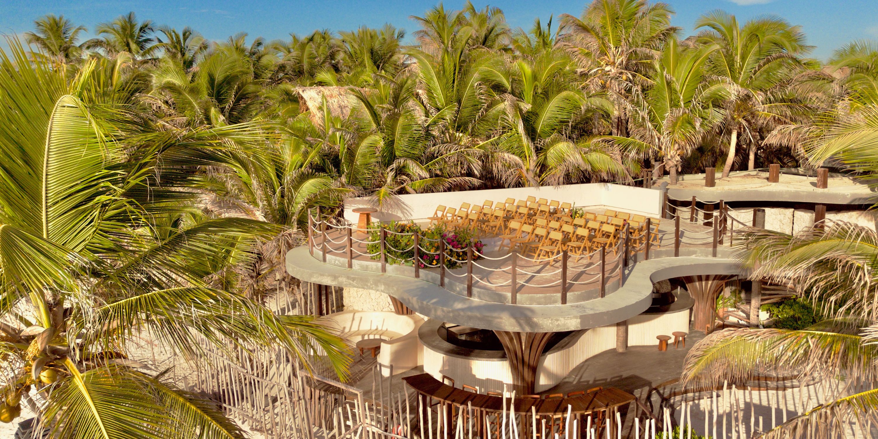 Open-air rooftop wedding venue with rows of chairs, set amid palm trees and lush tropical greenery.