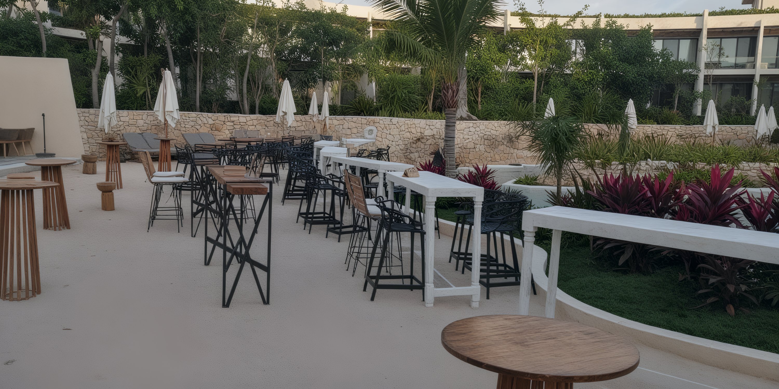 A picturesque outdoor patio perfect for a destination wedding, featuring tables and chairs arranged under elegant umbrellas and surrounded by lush greenery.